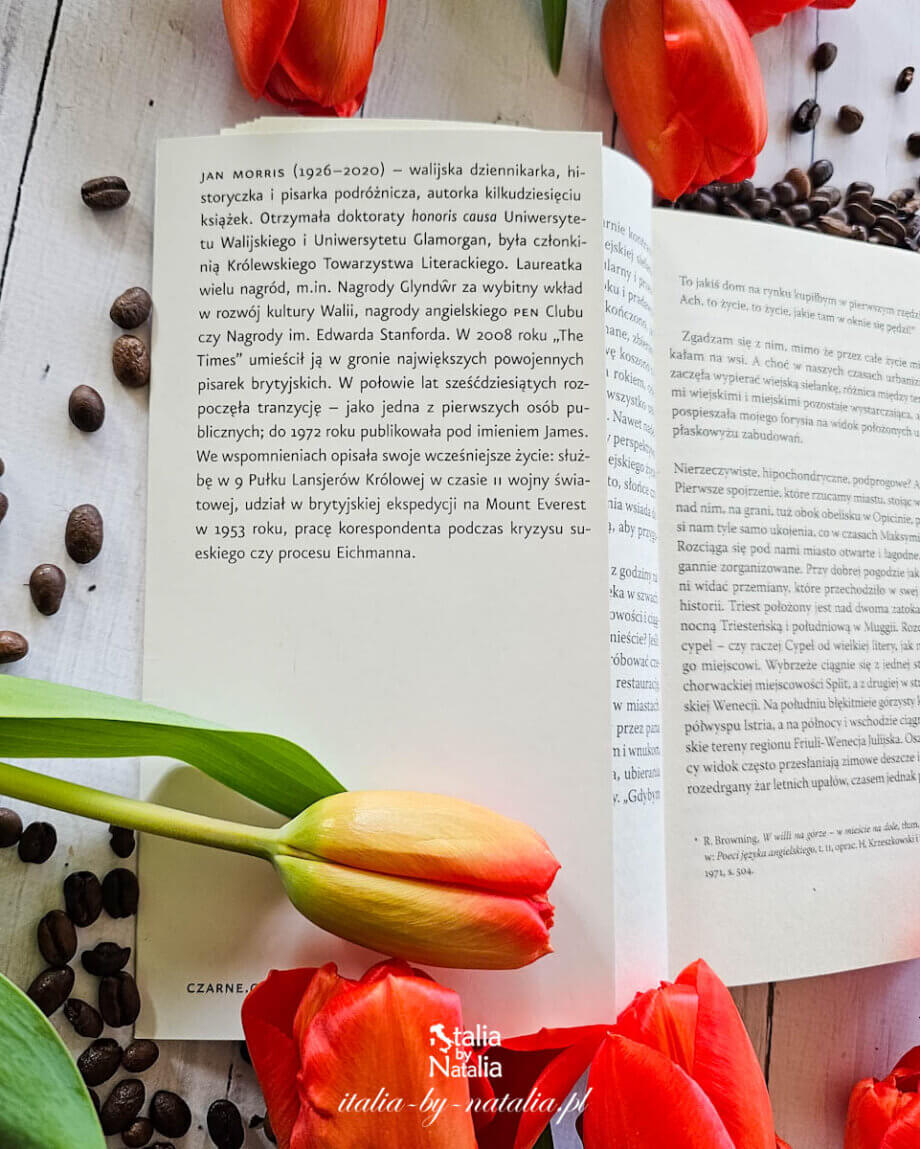 Otwarta książka „Triest, czyli nigdzie” Jana Morrisa z widoczną notą o autorze wśród tulipanów i rozsypanych ziaren kawy