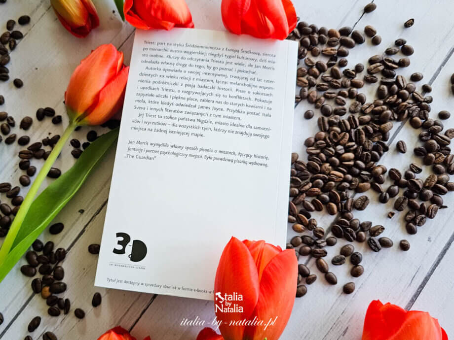 książka „Triest, czyli nigdzie” Jana Morrisa wśród tulipanów i rozsypanych ziaren kawy na jasnym drewnie